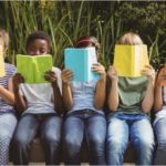 Group of young children reading books outside 